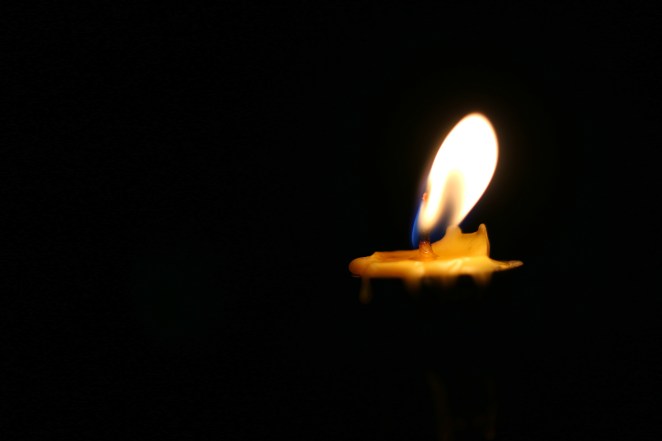 One or Single yellow light candle burning brightly in the black background, candle light isolated black in dark night.